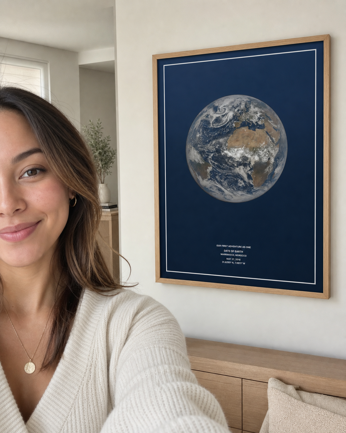 Woman taking a selfie beside a framed navy Date of Earth print at home.