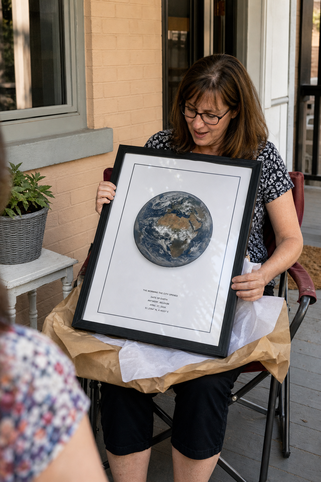 Woman opening a framed Date of Earth print on a front porch.